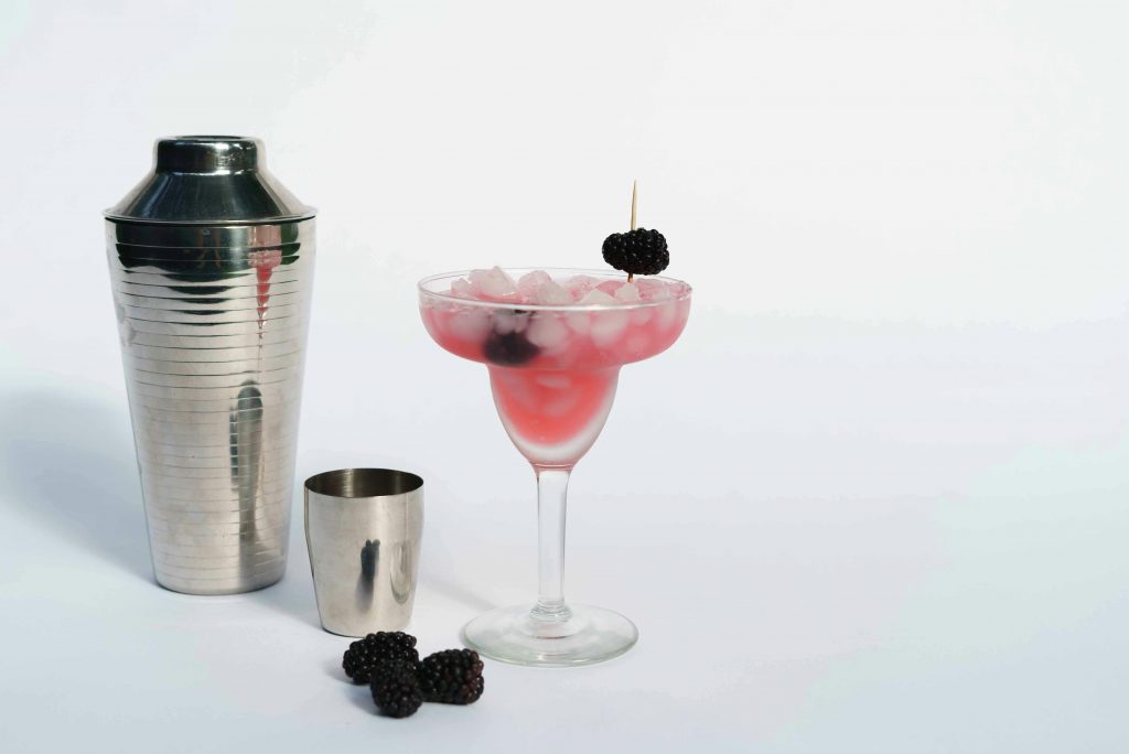 A cocktail shaker, jigger, and cocktail.