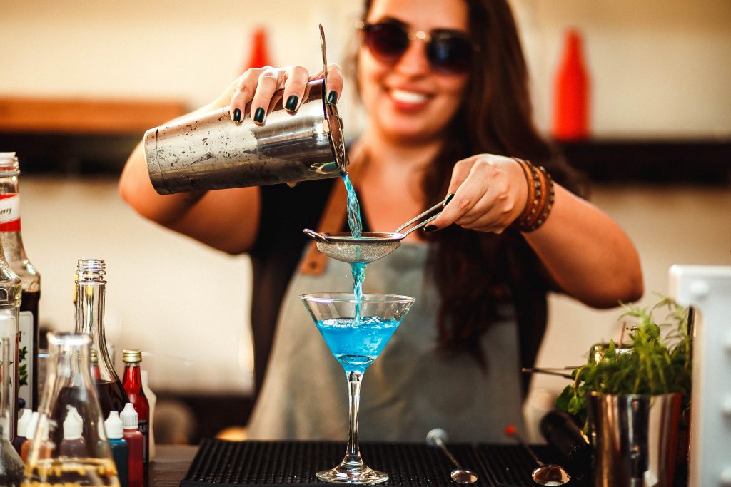 A bartender pouring a cocktail into a glass through a strainer