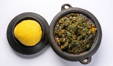 Efik Afang soup Nigerian served in a clay bowl with garri on a white background